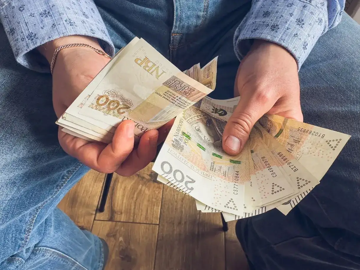 Dłonie trzymające stos banknot&oacute;w 200 zł, gotowe na dodatek urlopowy.