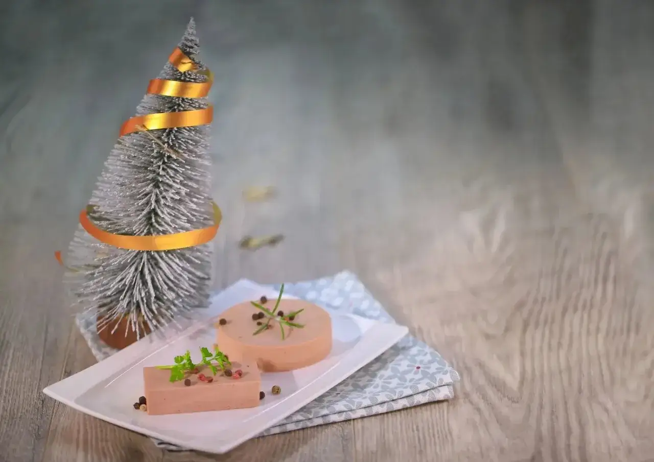 Une terrine de foie festive, d&eacute;cor&eacute;e de poivre et d'herbes, &agrave; c&ocirc;t&eacute; d'un sapin argent&eacute; orn&eacute; d'un ruban dor&eacute;.