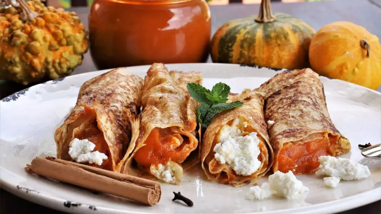 Rollitos de crepes rellenos de calabaza y queso fresco, decorados con menta. Ideales para recetas con calabaza.