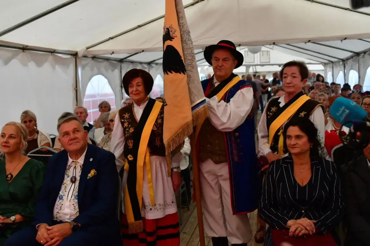 Ludzie w strojach ludowych, z flagą, celebrujący tradycję i gwarę kaszubską.