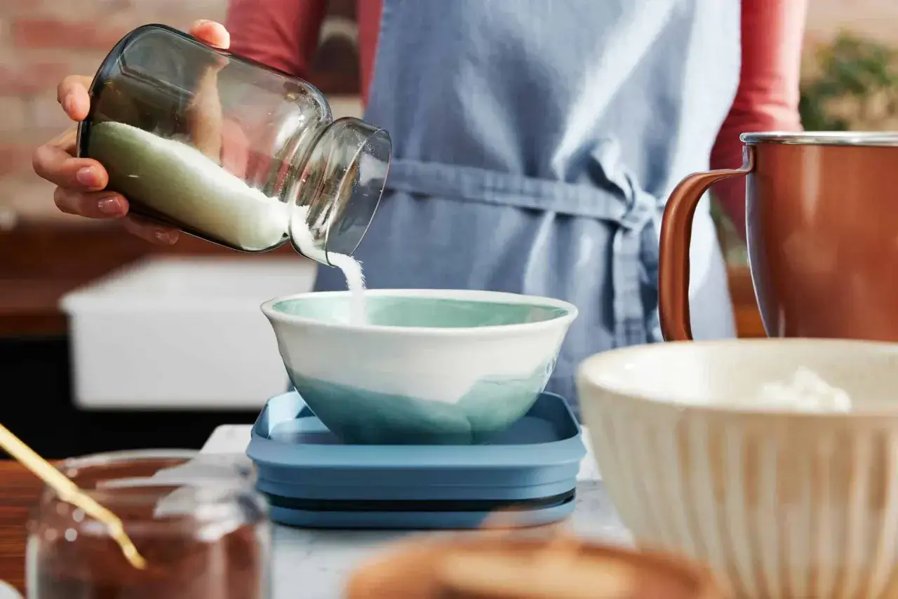 Eine Hand sch&uuml;ttet Zucker aus einem Glas in eine Sch&uuml;ssel. Die Frage, wie viel Gramm Mehl in eine Tasse passen, besch&auml;ftigt viele B&auml;cker.
