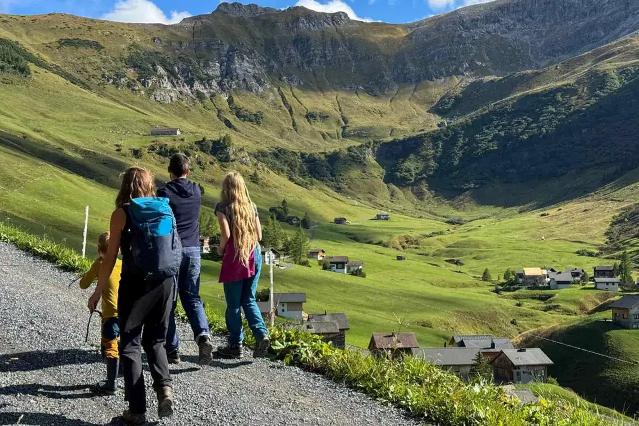 Familie genießt das Liechtenstein wandern in einer malerischen Berglandschaft mit kleinen Häusern und grünen Hängen.