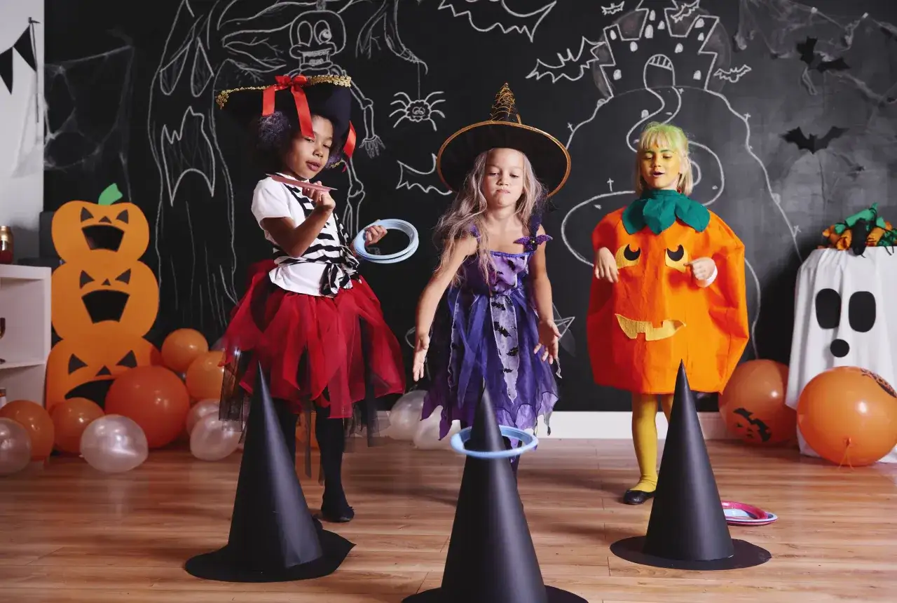 Niñas disfrutan de una divertida celebración de Halloween, jugando a lanzar aros en un ambiente decorado con calabazas y fantasmas.