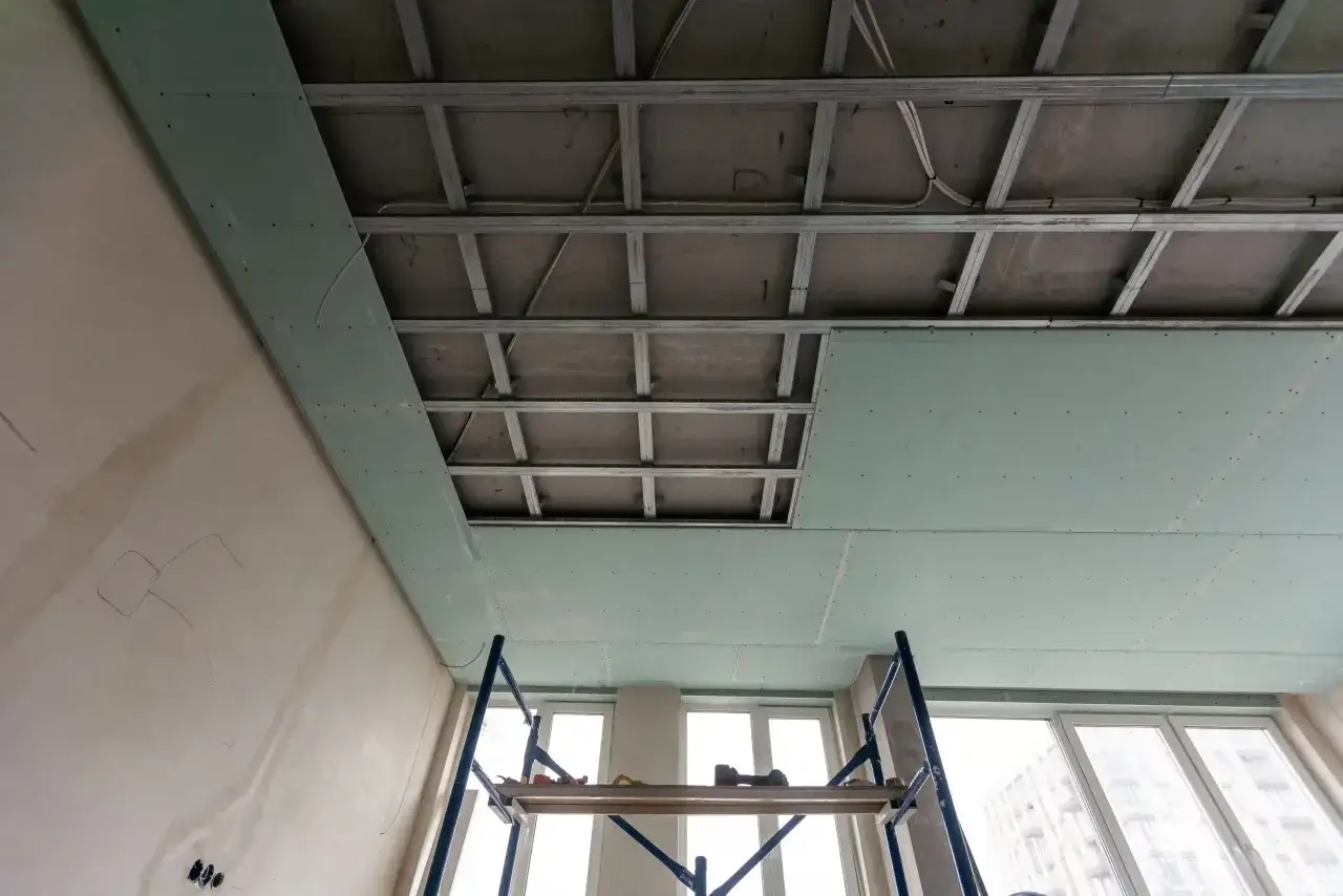 Instalaci&oacute;n de falso techo de pladur para aislar techo ruido vecinos. Andamio y estructura met&aacute;lica visibles.