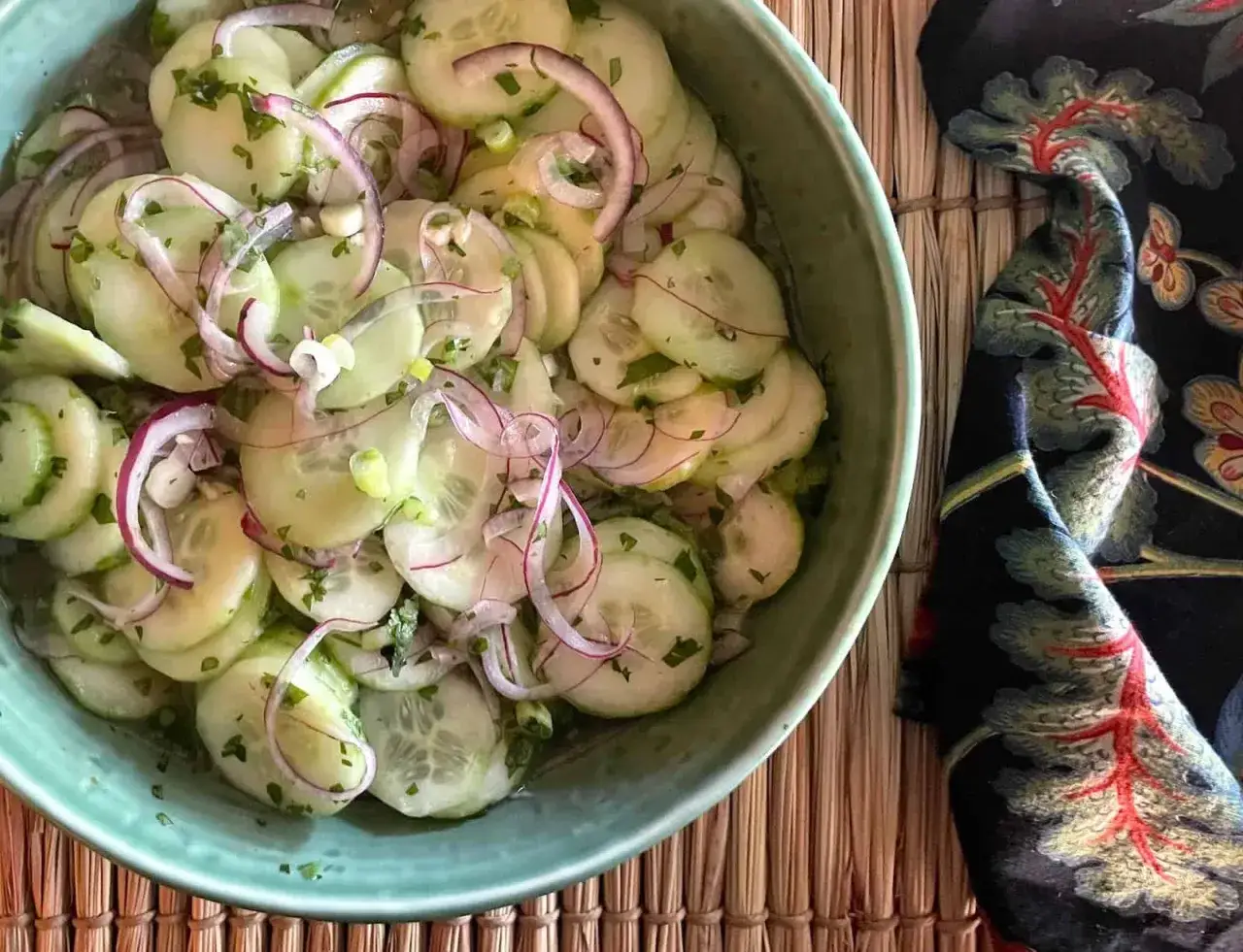 Frischer asiatischer Gurkensalat mit roten Zwiebeln und Kräutern in einer grünen Schüssel.