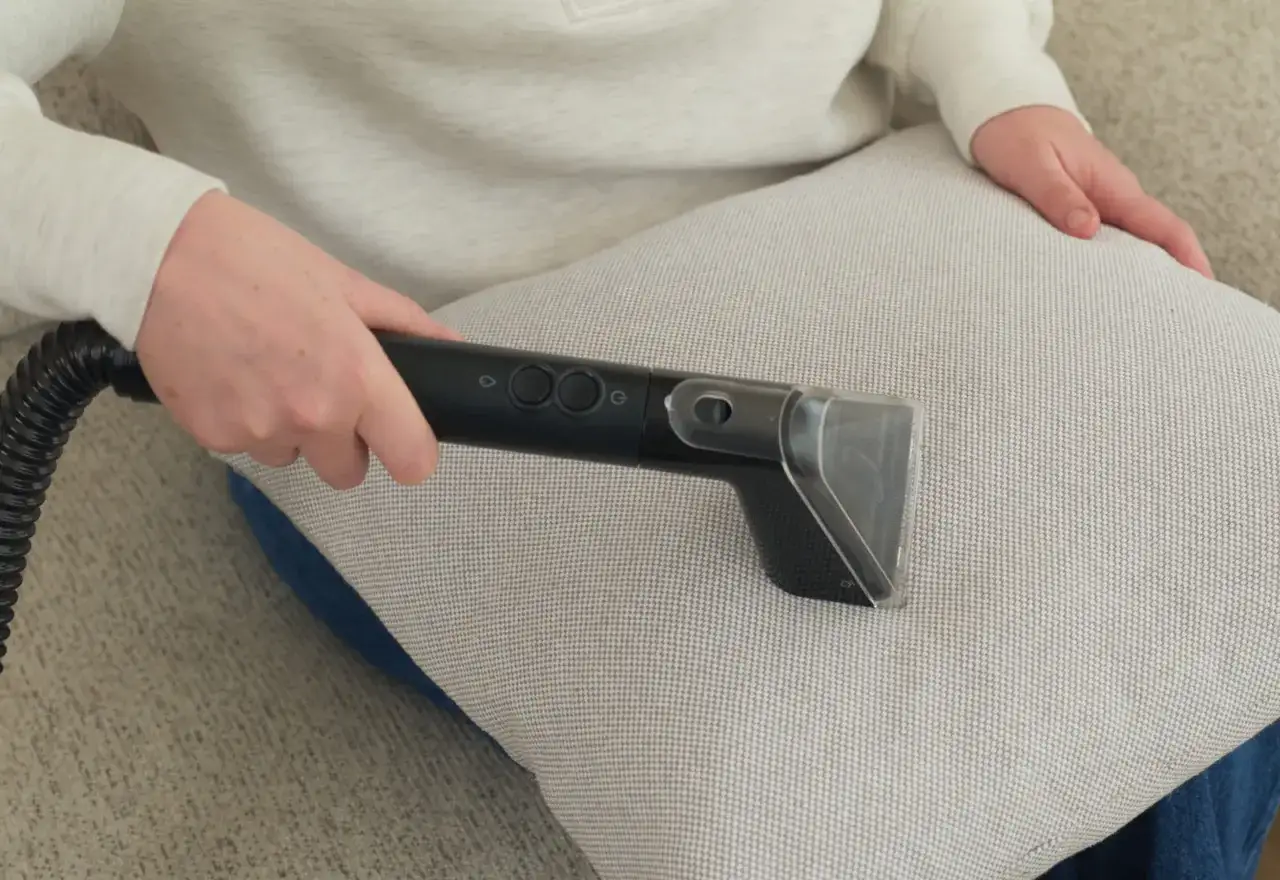 Person reng&ouml;r soffkudde med en textilv&aring;rdsmaskin, som om de skulle byta stoppning soffa.