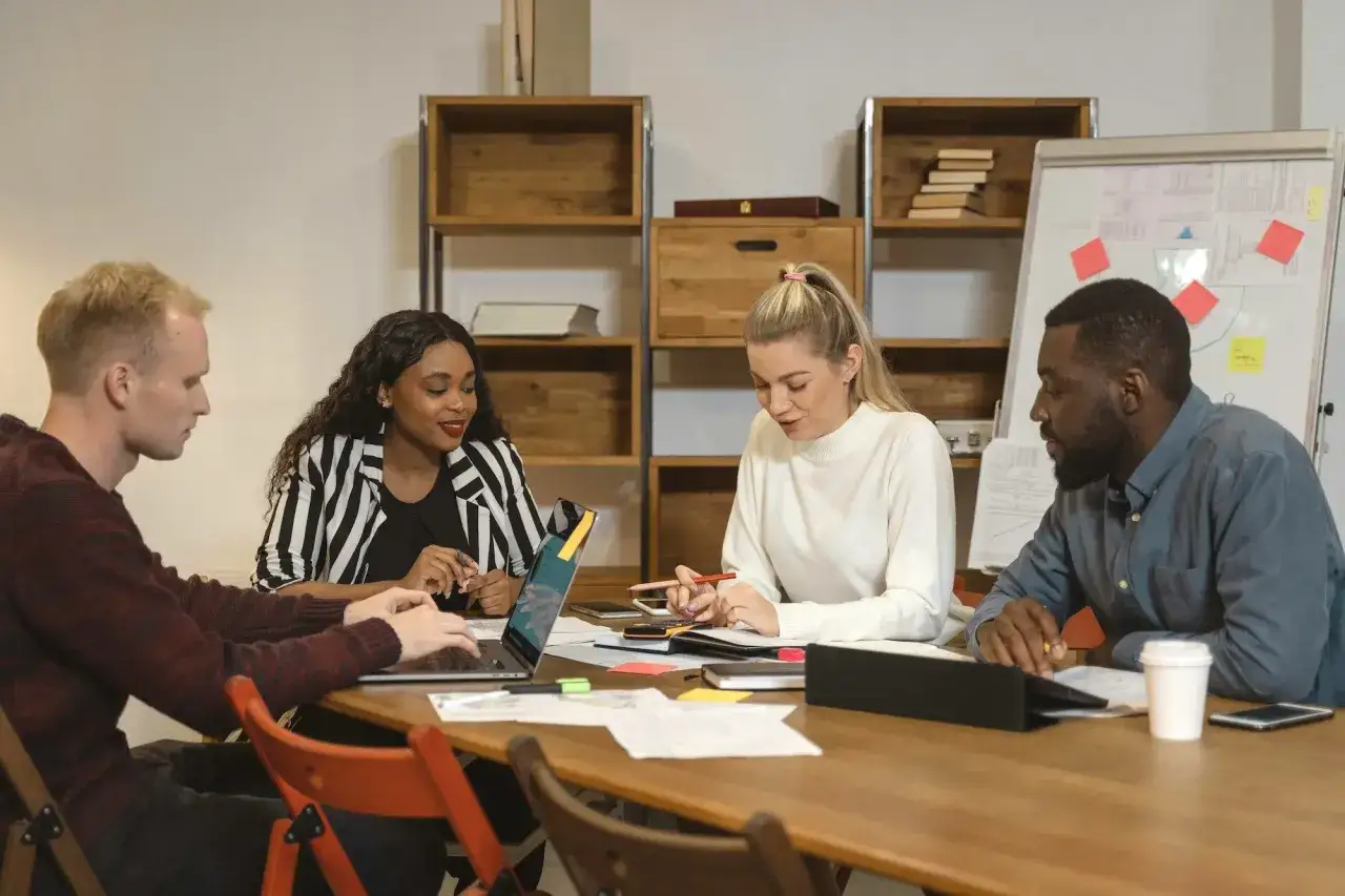 Four colleagues collaborate on a DEI certificate program online, discussing ideas around a table with laptops and notes.