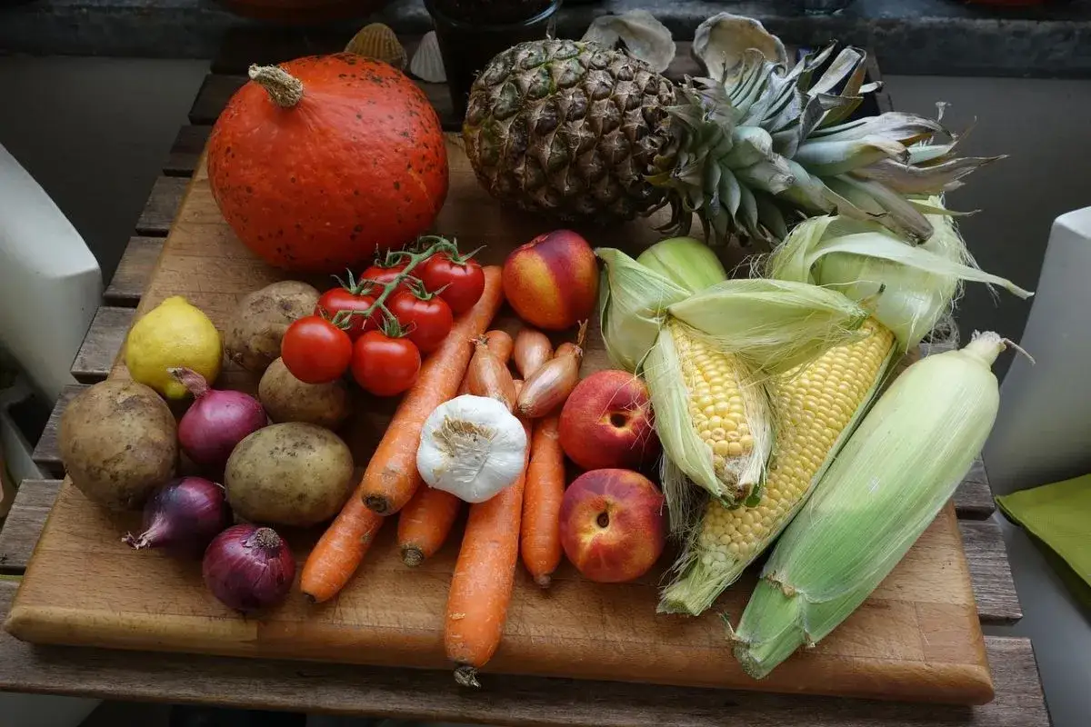 R&oacute;żnica między owocem a warzywem? Na desce dynia, ananas, pomidory, kukurydza, ziemniaki, marchewki, czosnek, cebula, cytryna i nektarynki.