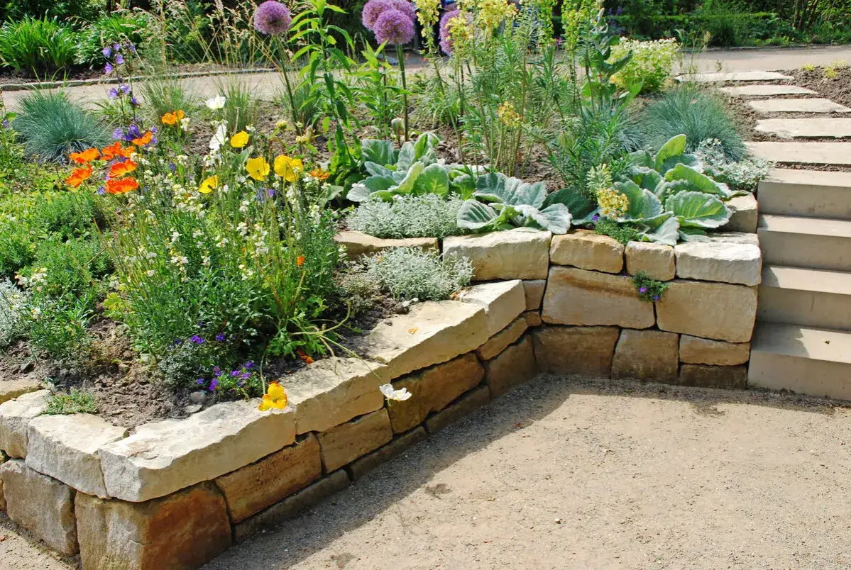 Blumenbeet mit bunten Blüten, Ziergräsern und einer Natursteinmauer. Tolle garten ideen für Hanglagen und Terrassierungen.