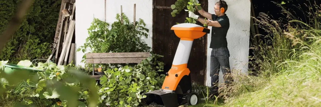 Mann mit Gehörschutz und Schutzbrille bedient einen orange-weißen meister shredder im Garten.