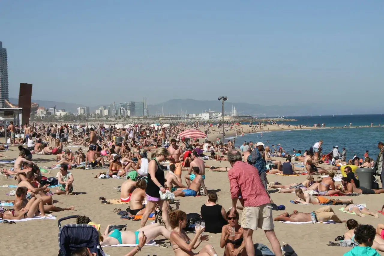 Tłum ludzi na plaży w Barcelonie. Czy w Hiszpanii jest drogo? Turyści odpoczywają, opalają się i kąpią w morzu.