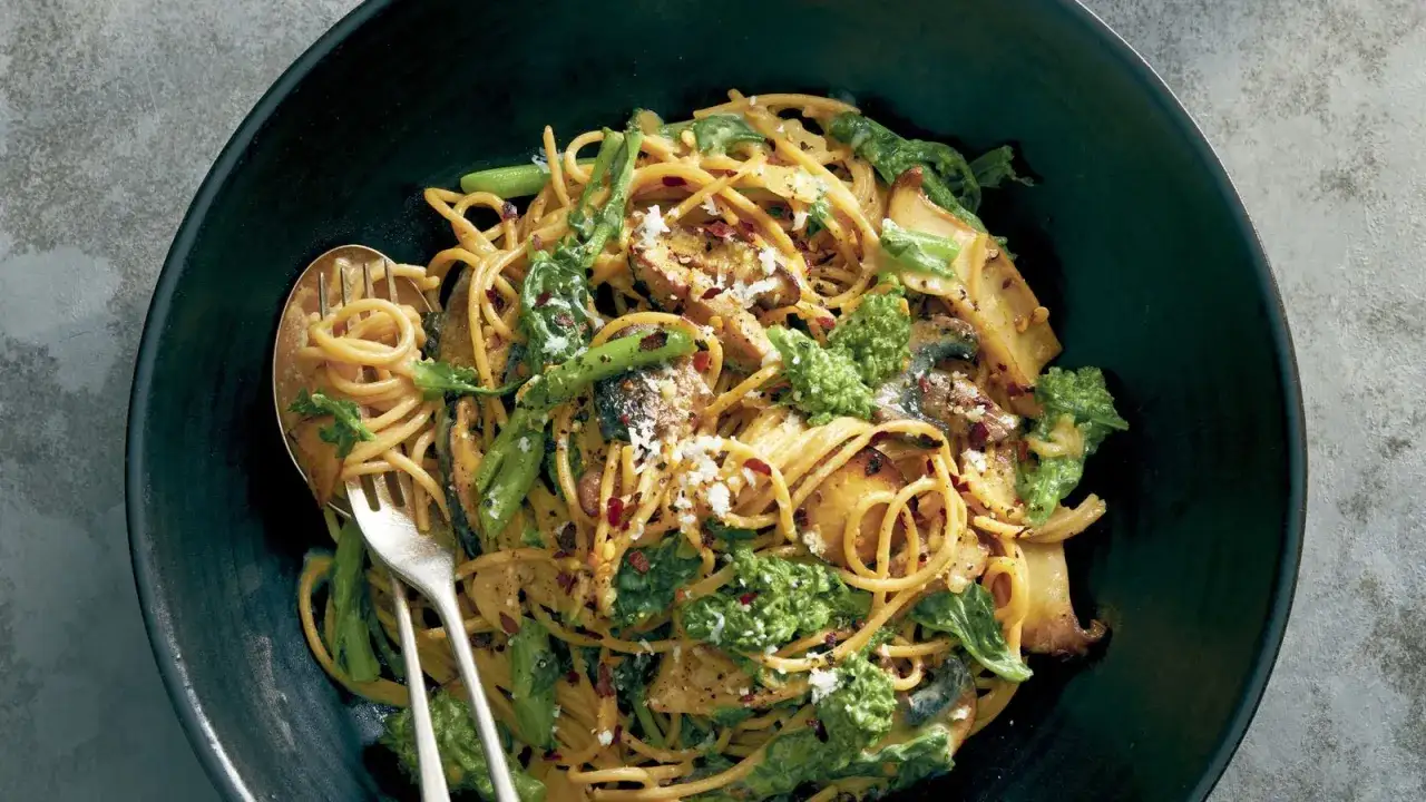 Un plat de pâtes carbonara vege, garni de brocolis, champignons et flocons de piment rouge, servi dans un bol noir avec une fourchette.