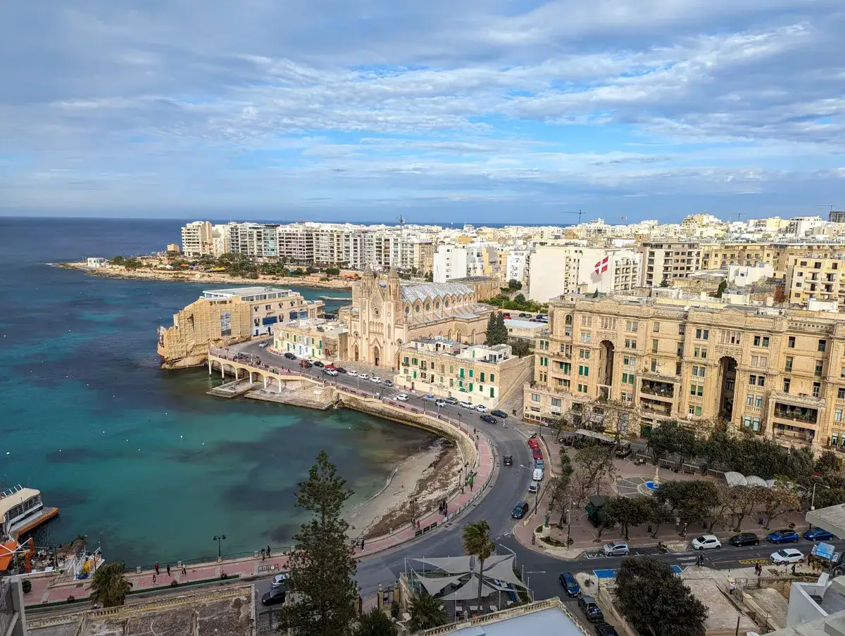 Malta im Dezember: Ein Blick auf die K&uuml;ste mit t&uuml;rkisfarbenem Wasser, einer Kirche und Geb&auml;uden. Das Wetter ist mild, ideal f&uuml;r einen Spaziergang.