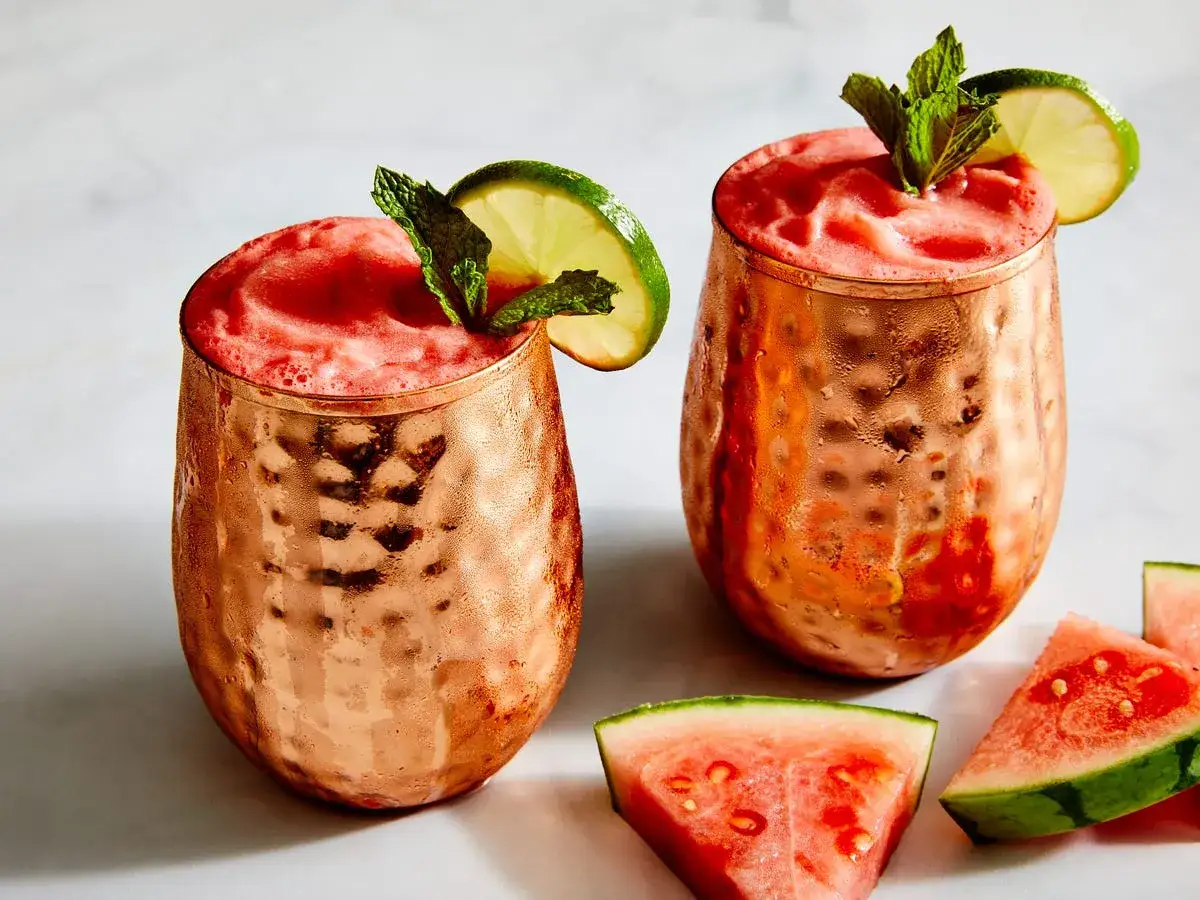 Tv&aring; frostiga koppar med rosa vodka drinkar, garnerade med lime och mynta. Vattenmelonbitar ligger bredvid.