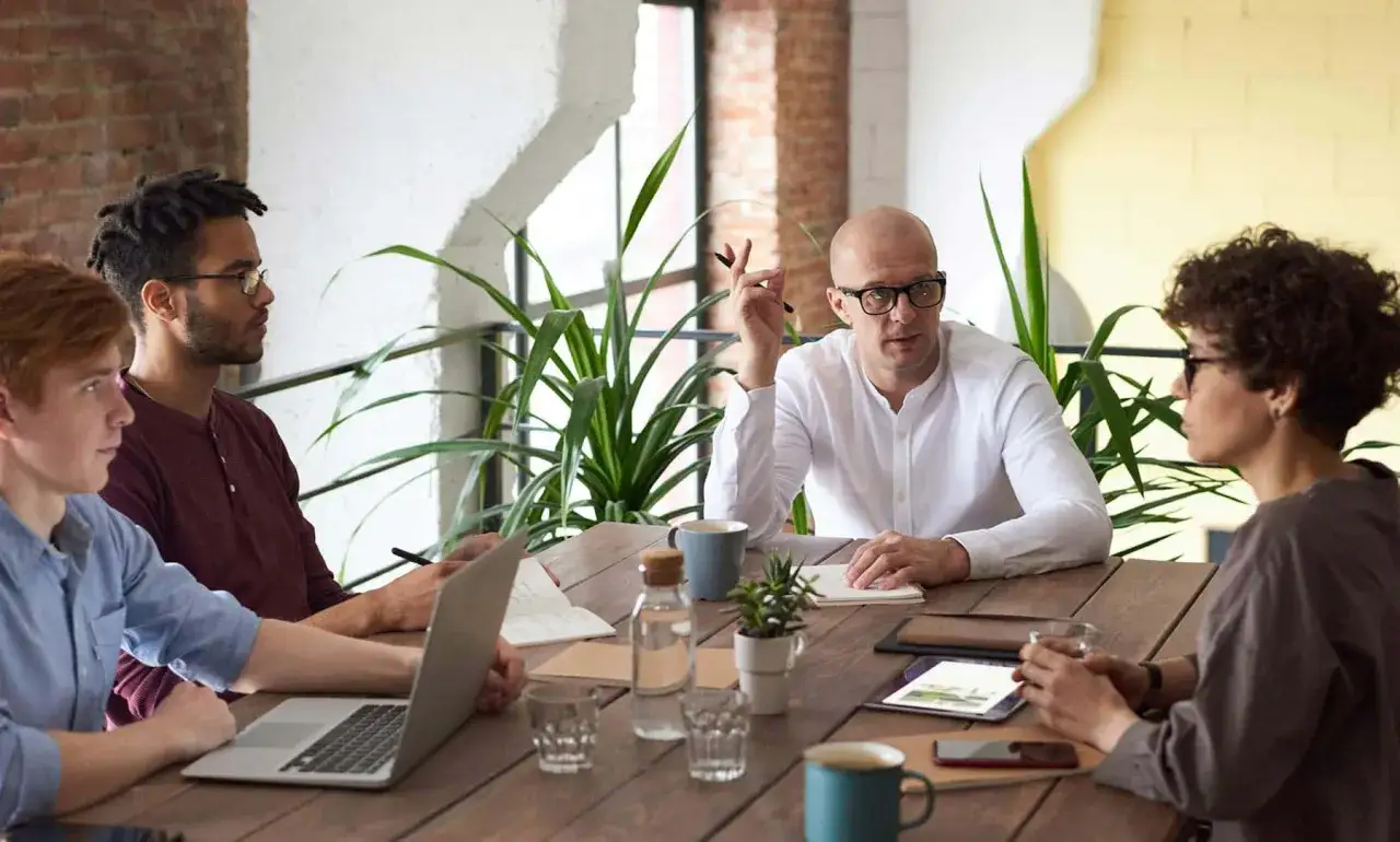 Equipo colaborando en una mesa de madera, demostrando excelentes **soft skills** de comunicaci&oacute;n y trabajo en equipo.