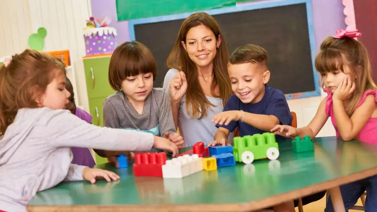 Lehrerin und Kinder bauen mit bunten Bausteinen. Das zeigt, was Elternarbeit in der Kita bedeutet: gemeinsames Lernen und Spielen.