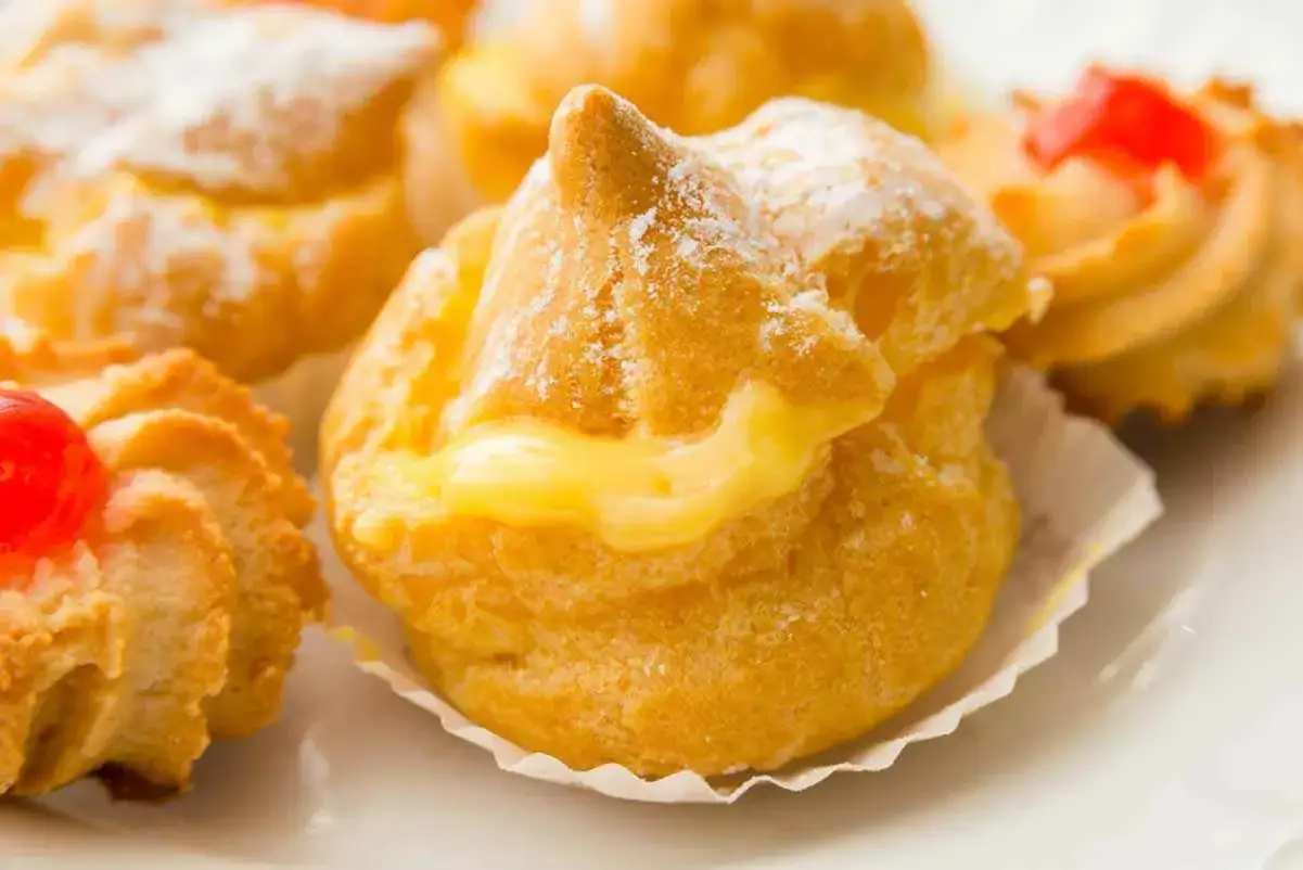 Bignè alla crema soffici e dorati, spolverati di zucchero a velo, con un ripieno cremoso che cola.
