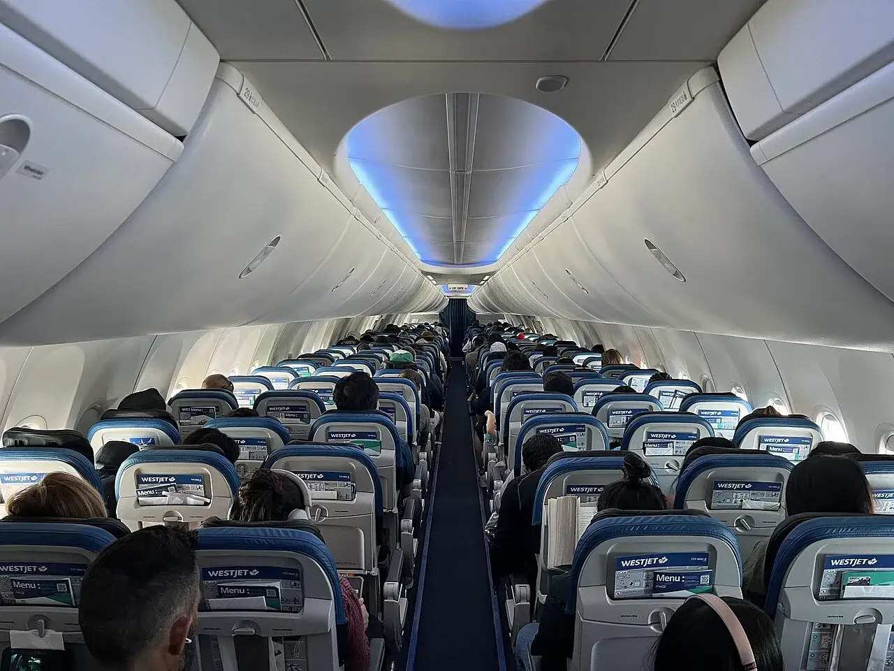 Wnętrze samolotu Boeing 737 MAX 8 linii WestJet, pełne pasażerów siedzących w rzędach.