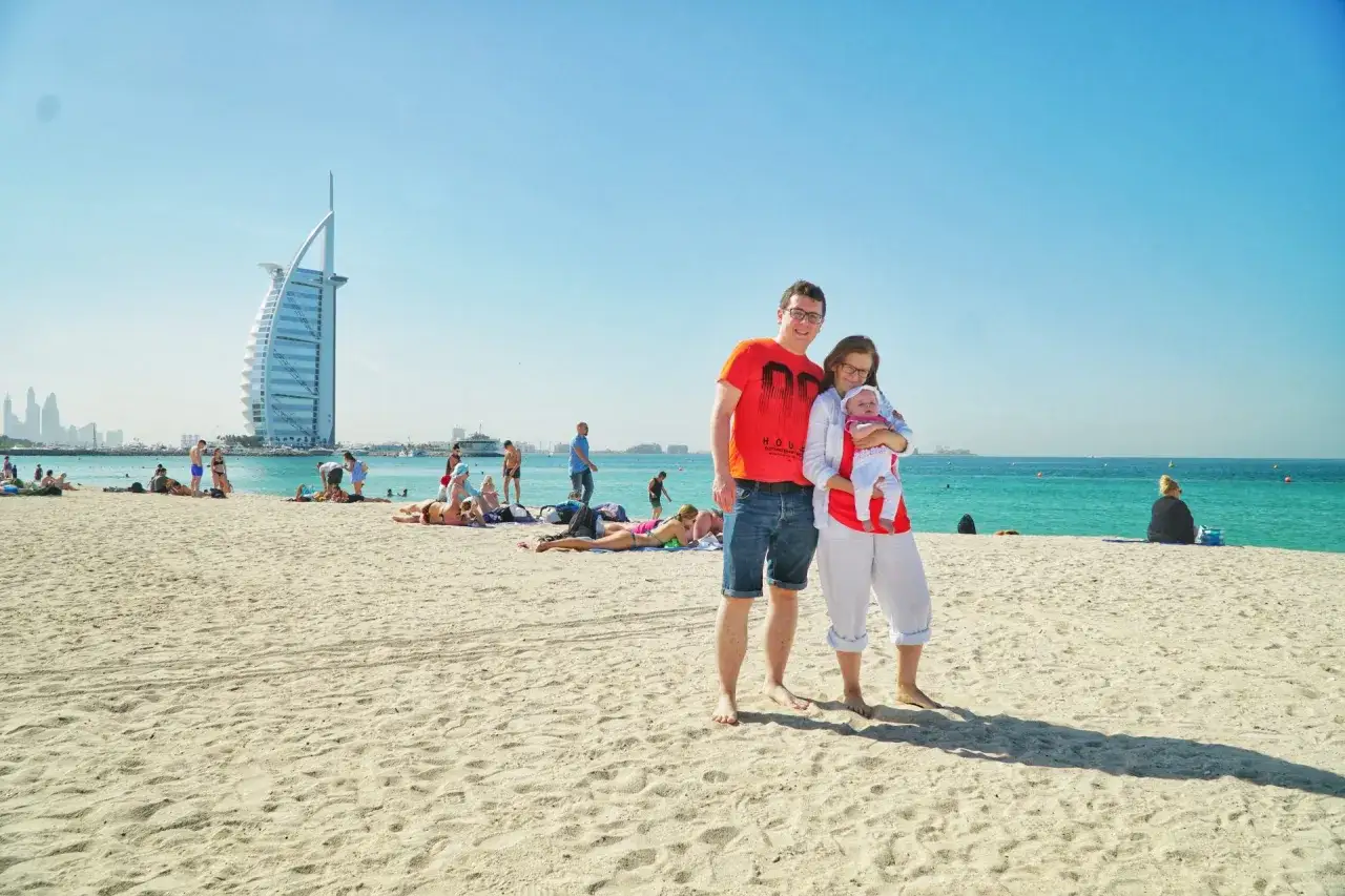 Rodzina cieszy się słońcem na plaży w Dubaju z dzieckiem. W tle widać słynny hotel Burj Al Arab.
