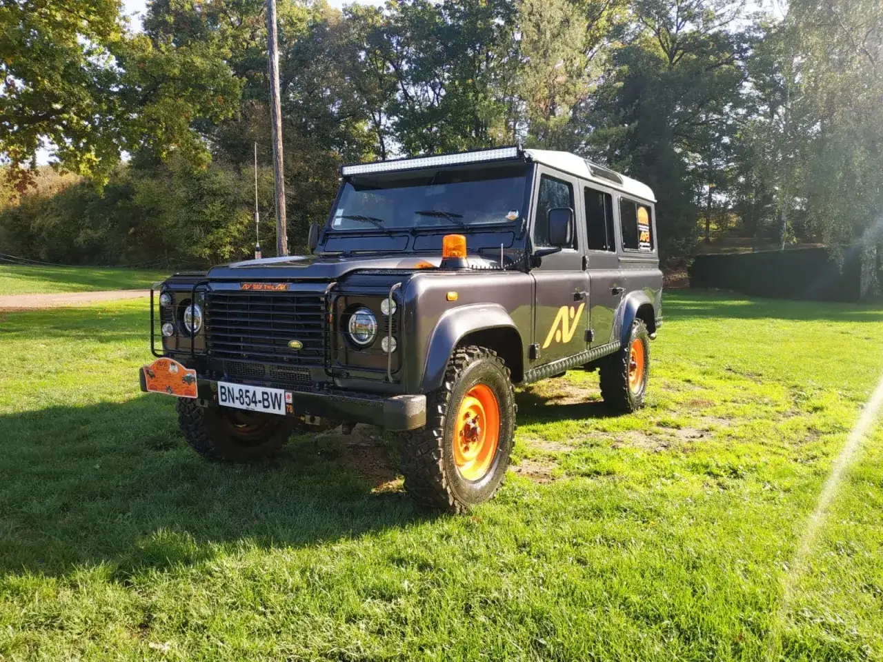 Le meilleur 4x4 tout-terrain, un Land Rover Defender gris avec jantes oranges, prêt pour l'aventure sur l'herbe.