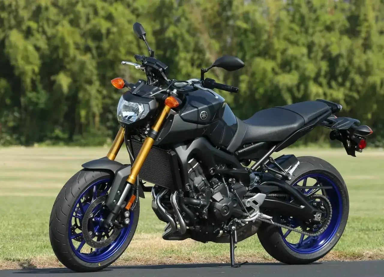 Czarny motocykl Yamaha MT09 z niebieskimi felgami stoi na tle zieleni.