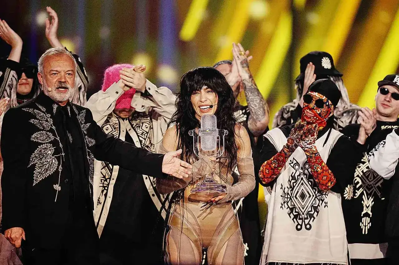Eurovision vinnare genom åren firas på scenen. En kvinna med mörkt hår håller i en mikrofonpokal, omgiven av jublande personer.