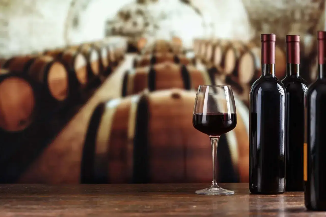 Glas Rotwein und Flaschen vor Reihen von Weinfässern in der Cantine San Marzano.