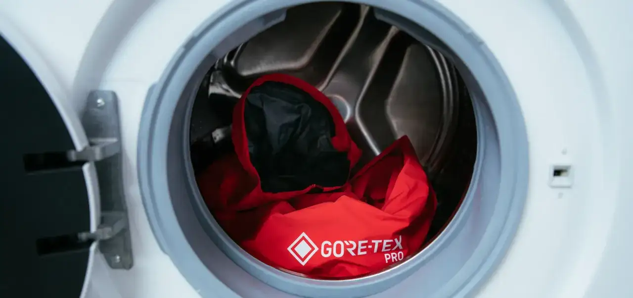 Chaqueta roja Gore-Tex Pro dentro de una lavadora, lista para el lavado. Aprende como lavar Gore-Tex para mantener su impermeabilidad.