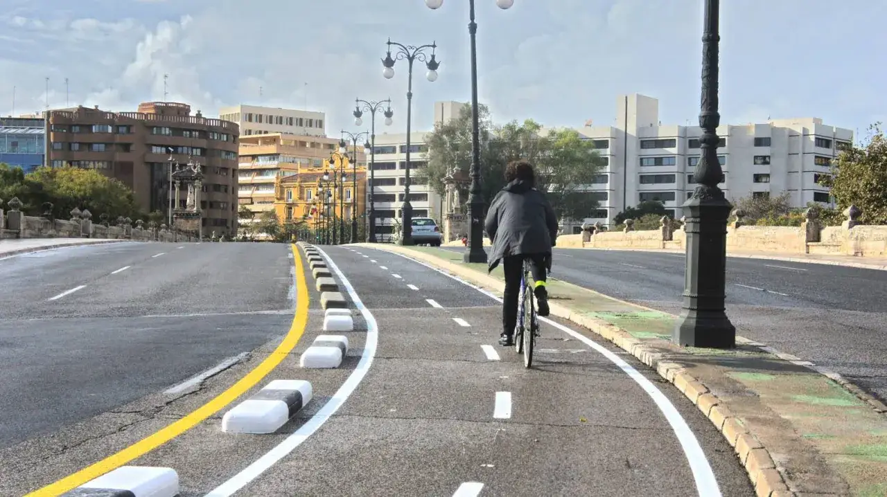 Persona ir en bicicleta por un carril bici en una ciudad, con edificios modernos y farolas a lo largo del camino.
