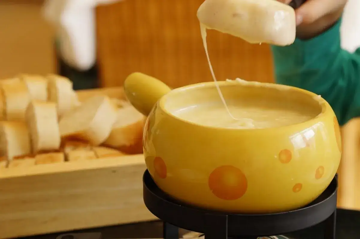 Un pezzo di pane viene intinto in una fonduta di formaggio filante, un modo delizioso per sciogliere il formaggio.
