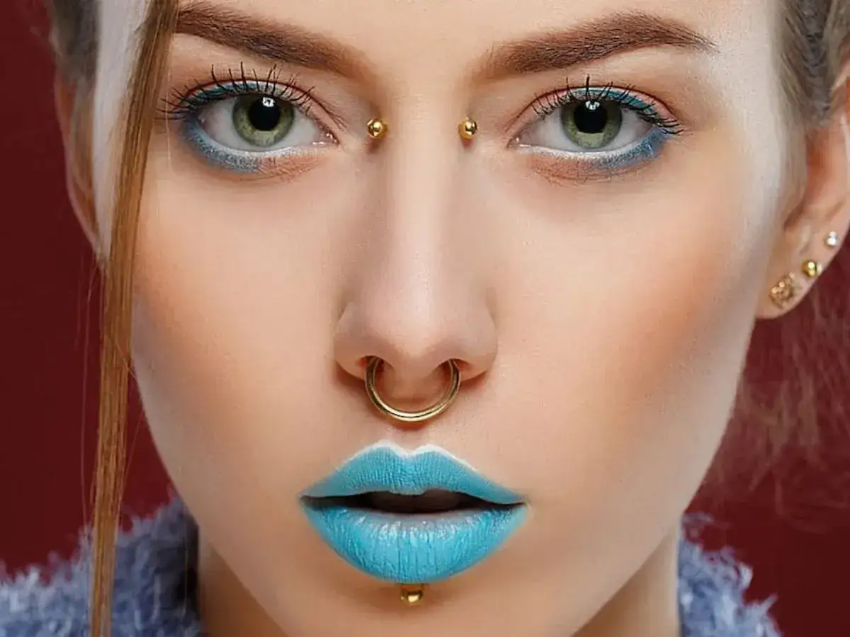Kobieta z błękitnymi ustami i kolczykami: septum, labret i bridge piercing.