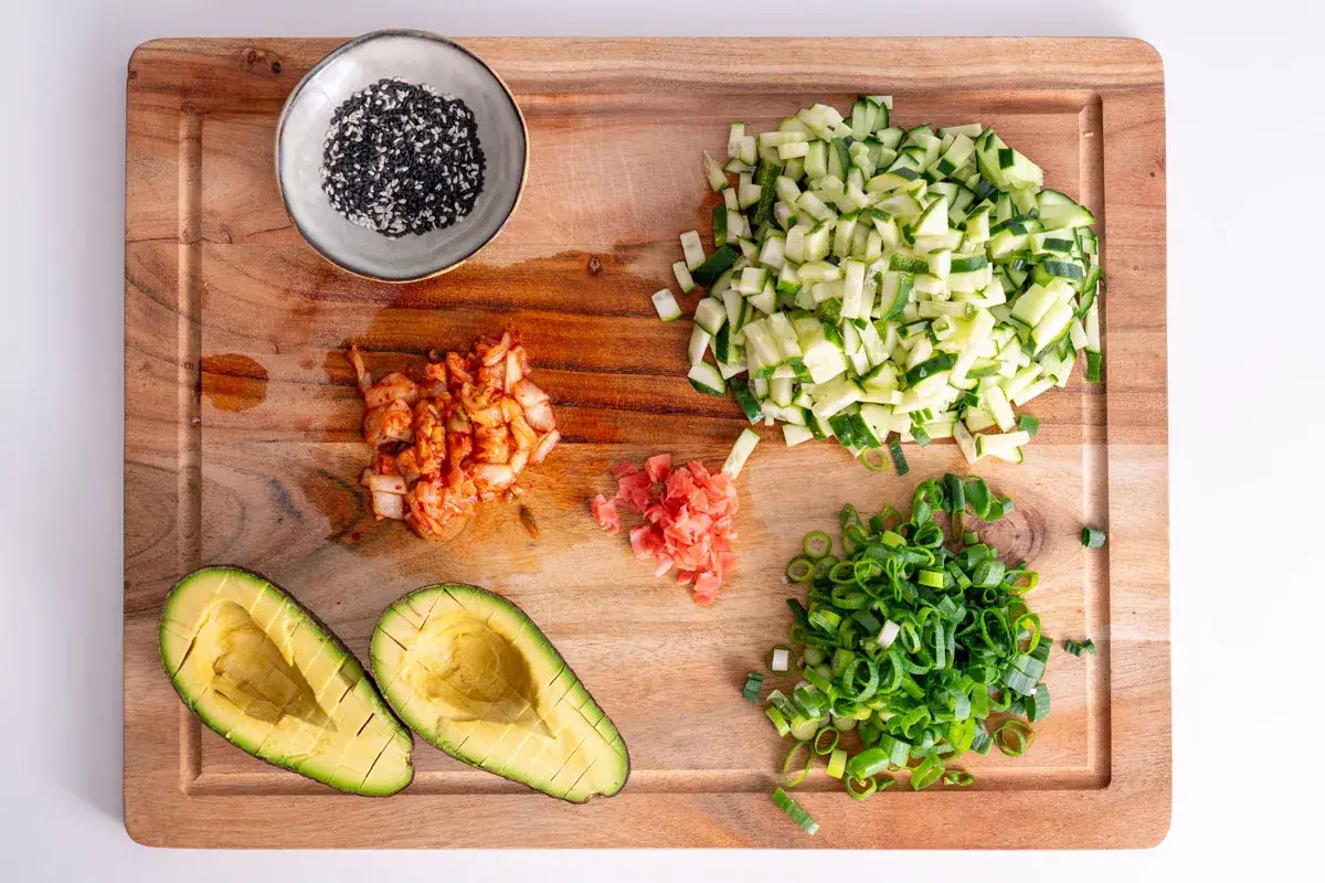Zutaten für eine vegane Sushi Bowl: Avocado, Gurke, Kimchi, Frühlingszwiebeln, Ingwer und Sesam.