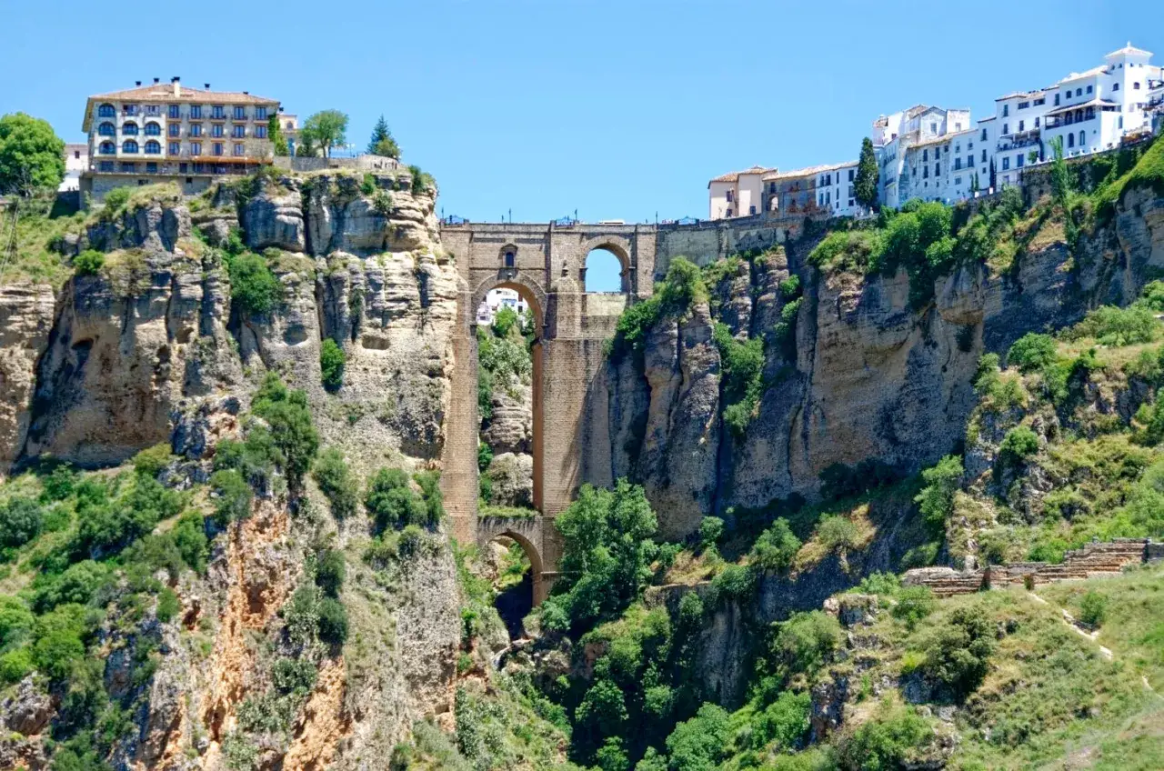 Impresionante puente de piedra sobre un profundo desfiladero, con casas blancas en la cima. Una **ruta** inolvidable por **Ronda**.