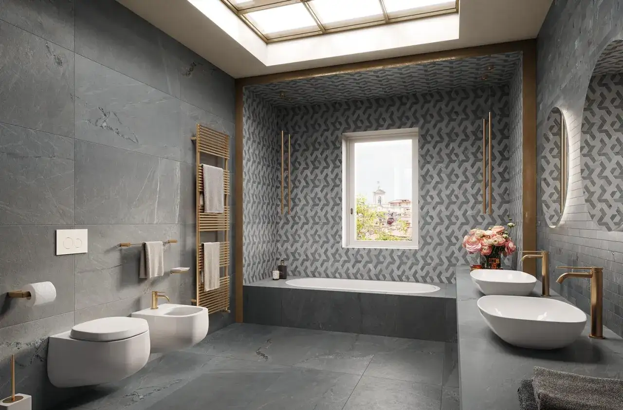 Salle de bain moderne avec wc suspendu, bidet, baignoire et double vasque. Le carrelage gris effet pierre contraste avec le motif géométrique sur le mur de la baignoire.