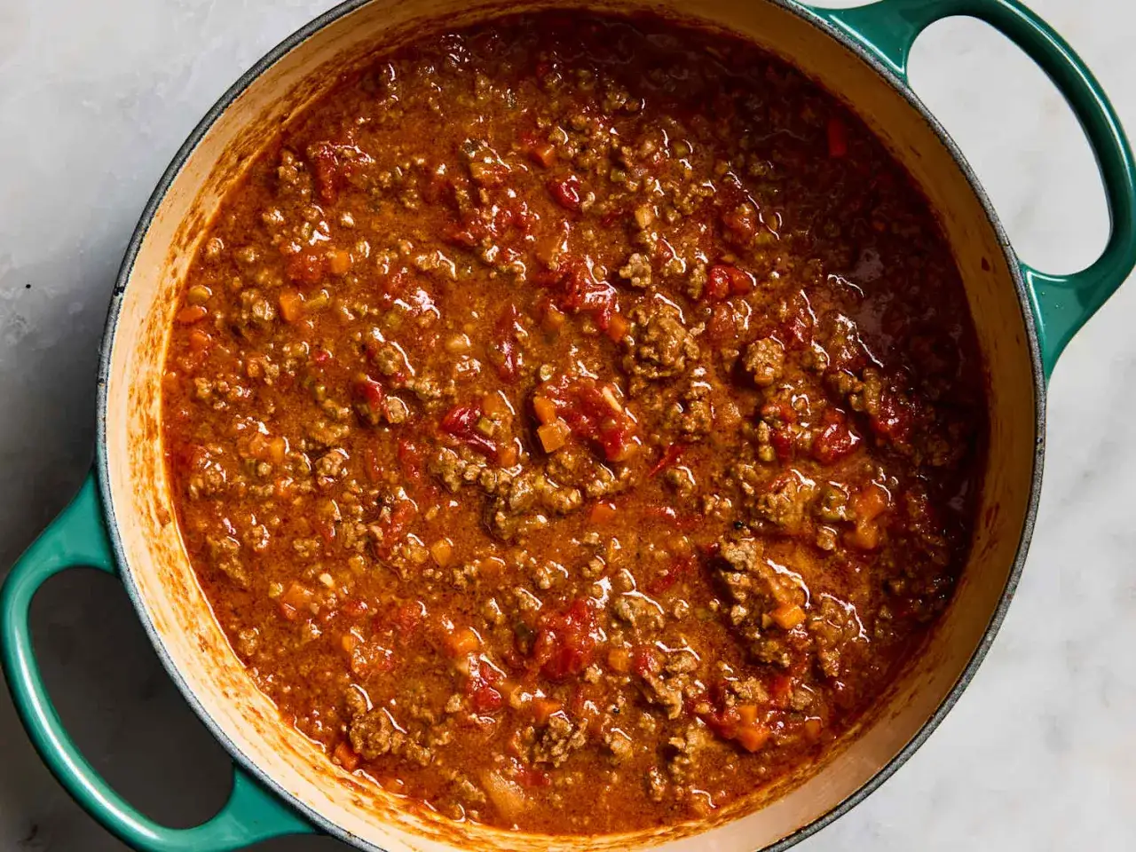 Herzhafte, **schnelle Bolognese** k&ouml;chelt in einem gr&uuml;nen Topf. Hackfleisch, Tomaten und Gem&uuml;se sind sichtbar.