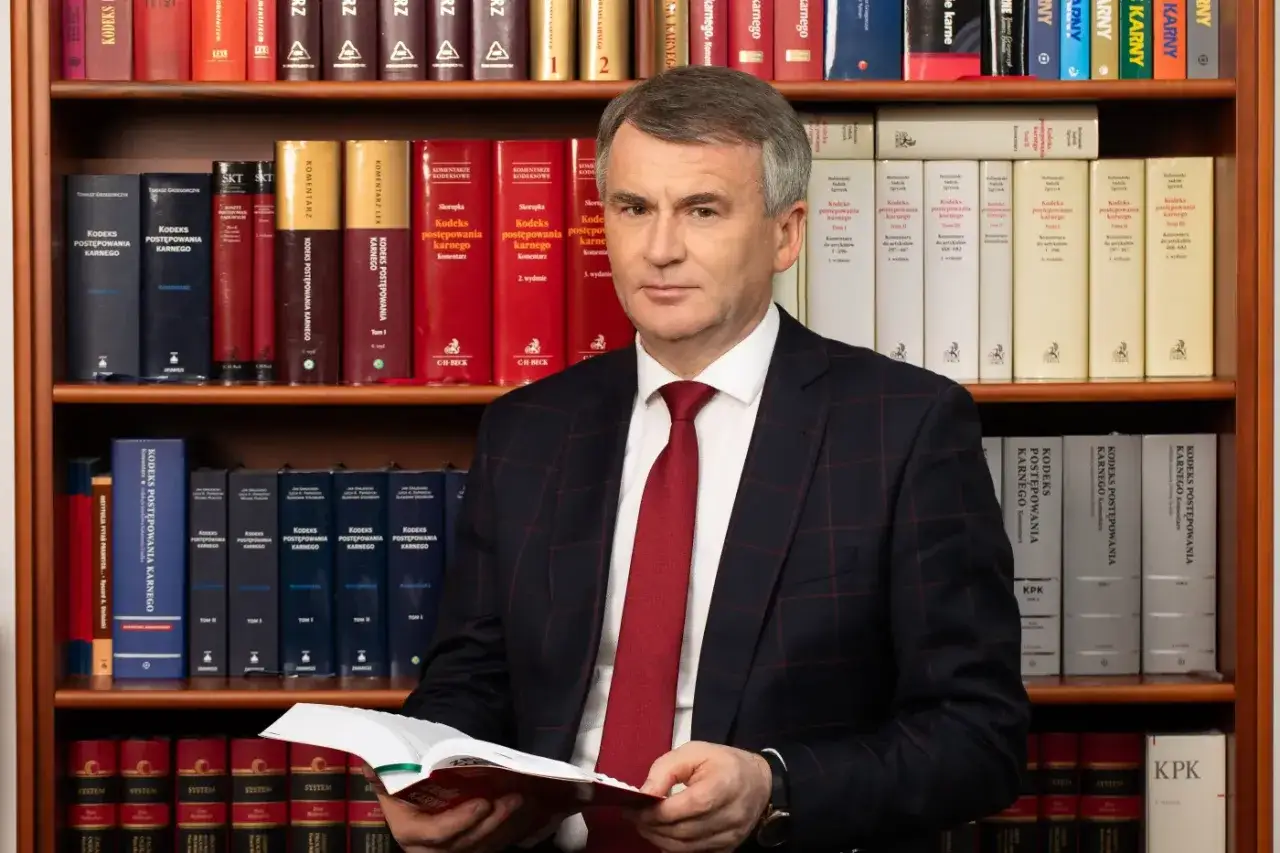Mężczyzna w garniturze przegląda Kodeks postępowania karnego, otoczony regałami pełnymi prawniczych tomów.