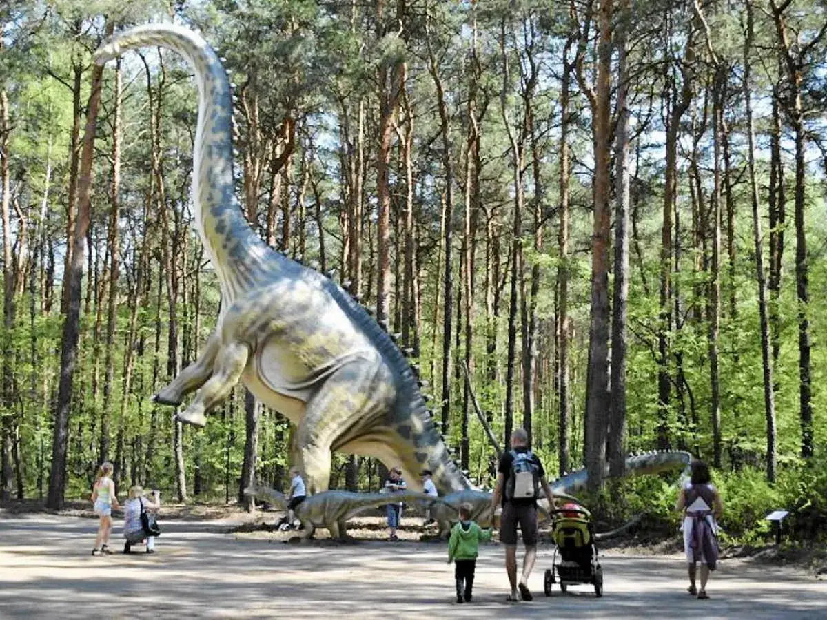 Rodzina spaceruje po największym parku w Polsce, podziwiając realistyczne modele dinozaurów wśród drzew.