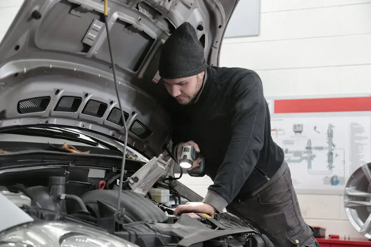 Elektromechanik samochodowy z latarką bada silnik. Zastanawiasz się, ile zarabia elektromechanik samochodowy?
