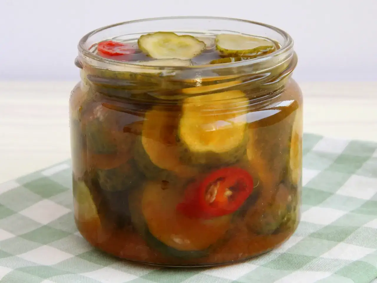 Słoik pełen małych og&oacute;rk&oacute;w z chili, zanurzonych w zalewie. Czerwone kawałki papryczki chili dodają pikantnego akcentu.