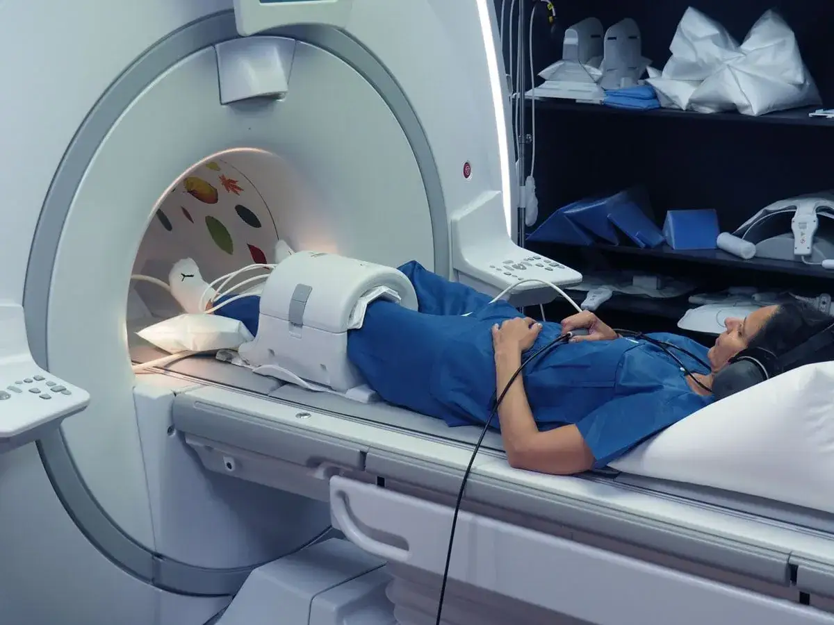Kobieta leży w aparacie do rezonansu magnetycznego, przygotowana do badania z kontrastem. Wnętrze tunelu ozdobione jest kolorowymi liśćmi.