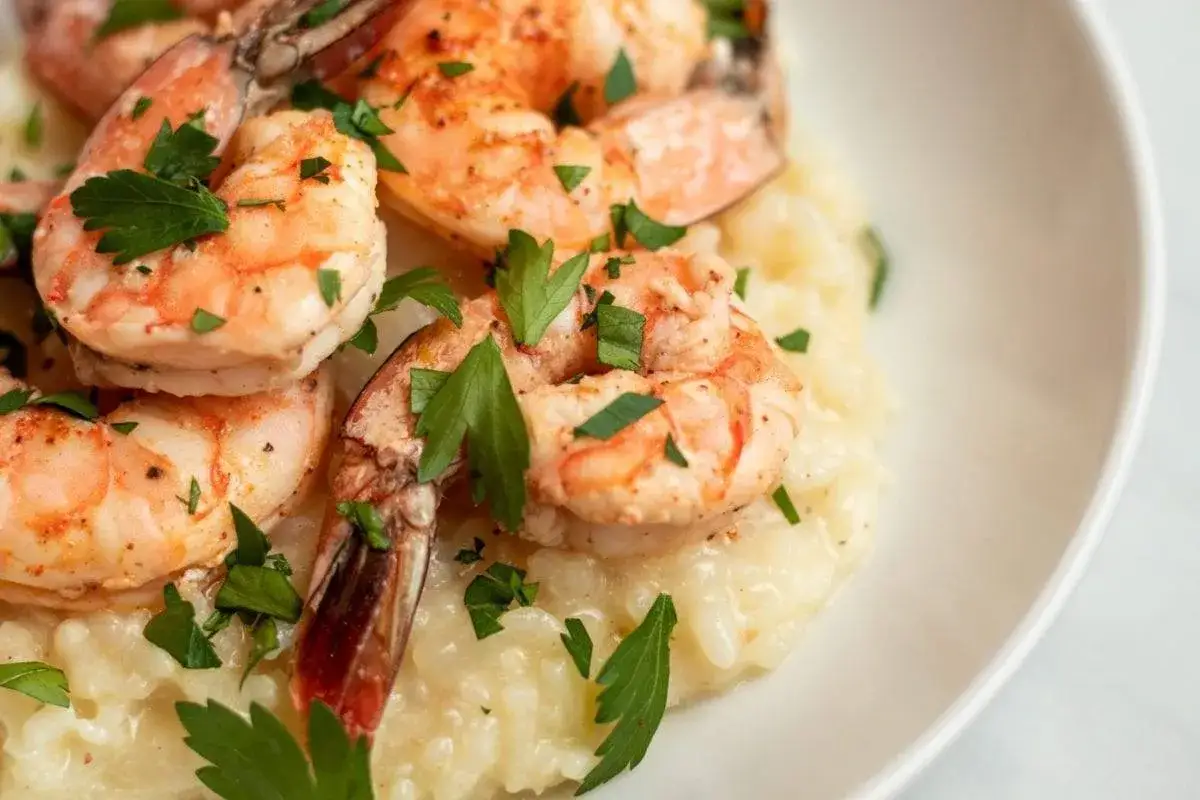 Pyszne risotto z krewetkami, udekorowane świeżą natką pietruszki, prezentuje się apetycznie na białym talerzu.