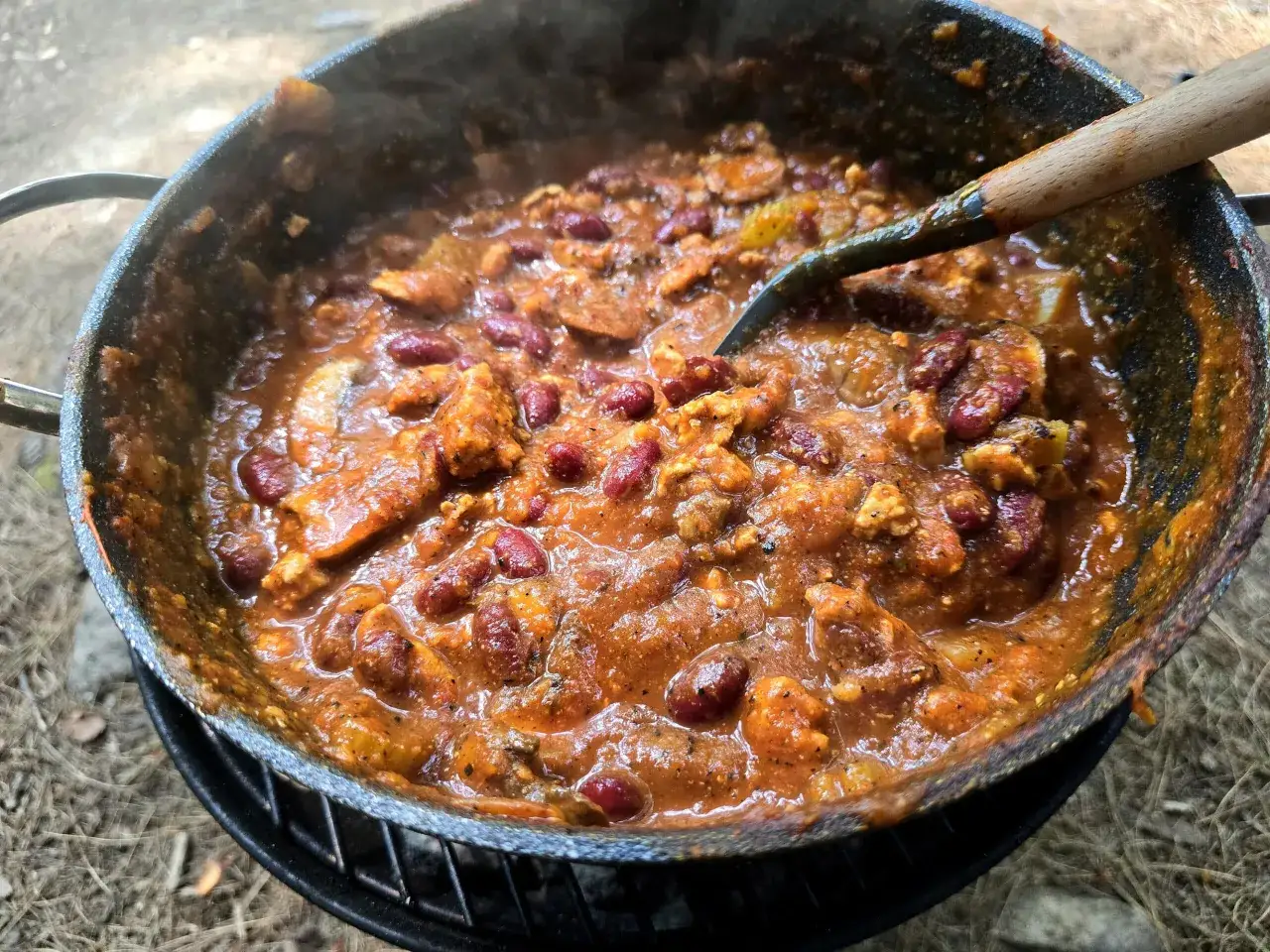 A hearty dutch oven chilli, bubbling with kidney beans and savory meat, is being stirred with a wooden spoon.
