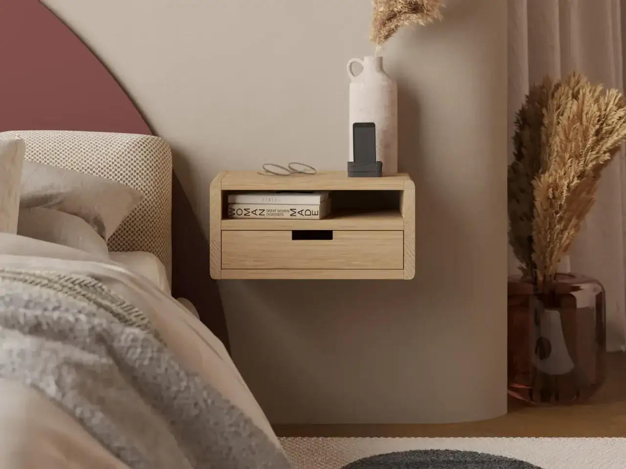 Minimalistyczna szafka nocna wisząca z drewna, z szufladą i otwartą półką, na której leżą okulary, telefon i książki.