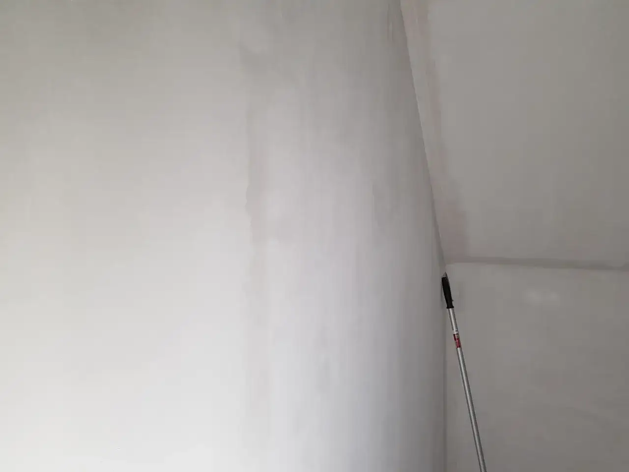 En lång skrapa står lutad mot en vit vägg i ett hörn. Förberedelser för att slipa innan målning.
