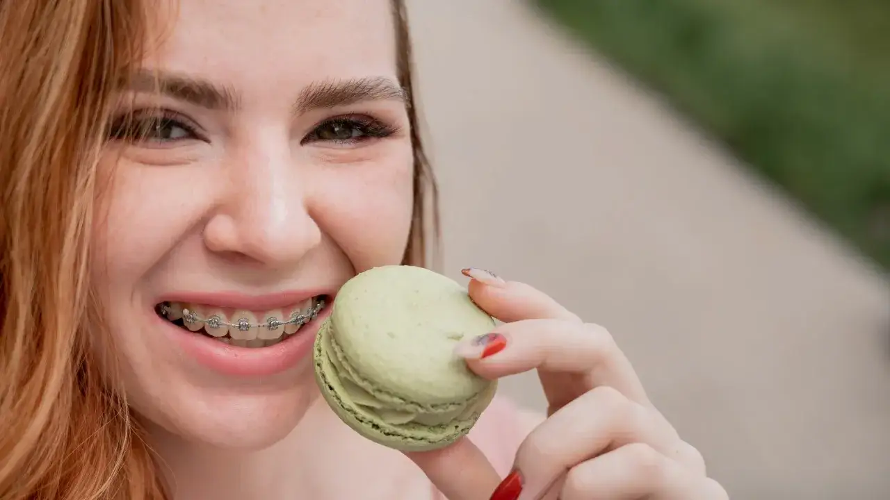 Uśmiechnięta dziewczyna z aparatem ortodontycznym trzyma makaronik. Nawet z aparatem można znaleźć przepisy na dietę.
