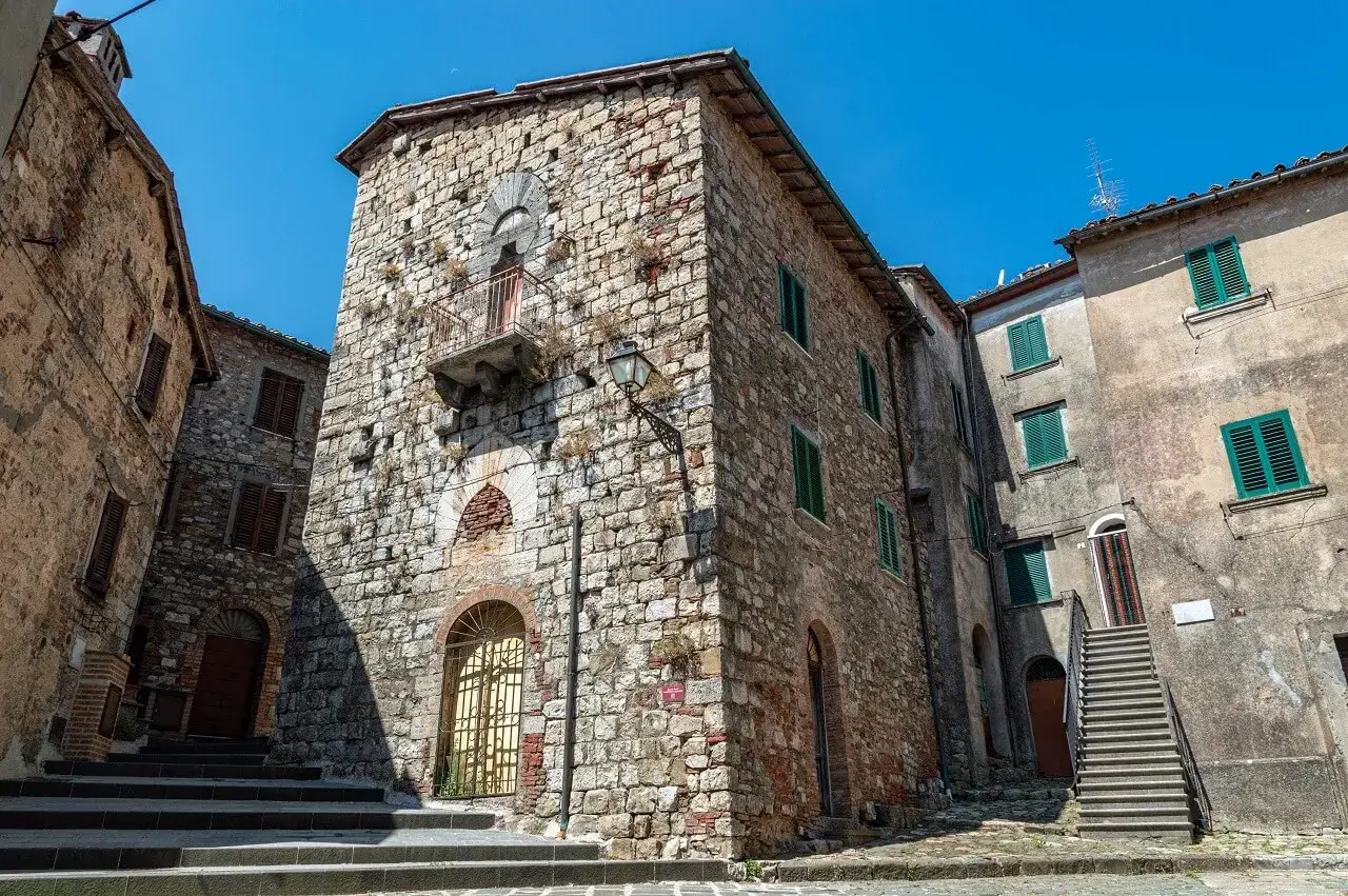 Antiche case in pietra a Montieri, cosa vedere: un vicolo con scale e balcone medievale sotto un cielo azzurro.