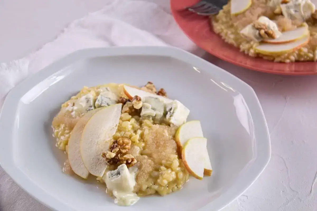 Un crémeux risotto poire gorgonzola, garni de noix et de fines tranches de poire, sur une assiette blanche.