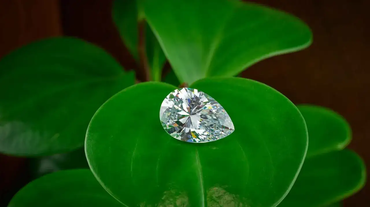 Un brillante diamante etico a forma di goccia riposa su foglie verdi lussureggianti, simbolo di purezza e responsabilit&agrave;.