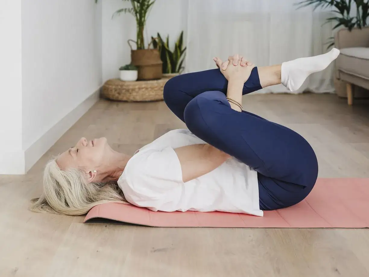 Femme en pr&eacute;menopause soulage son mal au ventre par des exercices doux sur un tapis rose.