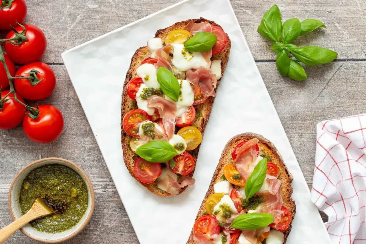 Deux bruschettas gourmandes garnies de tomates, mozzarella, jambon cru et d'un généreux filet de pesto.